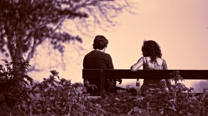 Casal triste sentado em um banco de praça, vistos por trás.