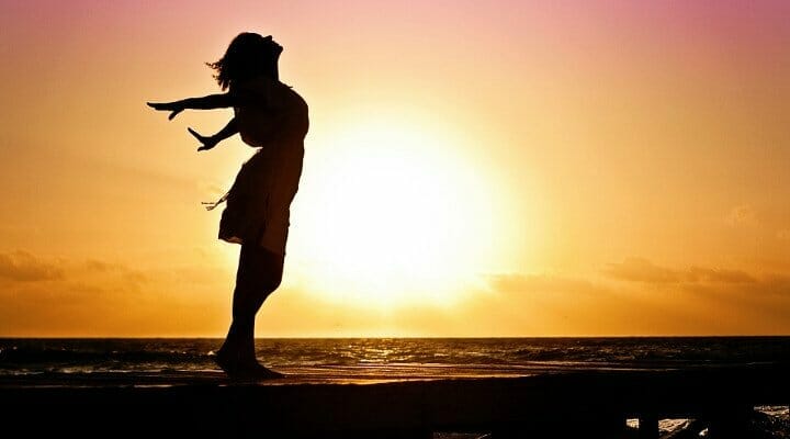 Contorno de uma mulher na praia com o sol ao fundo, mostrando-se feliz