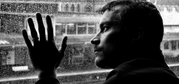 Homem deprimido olhando pela janela em dia chuvoso