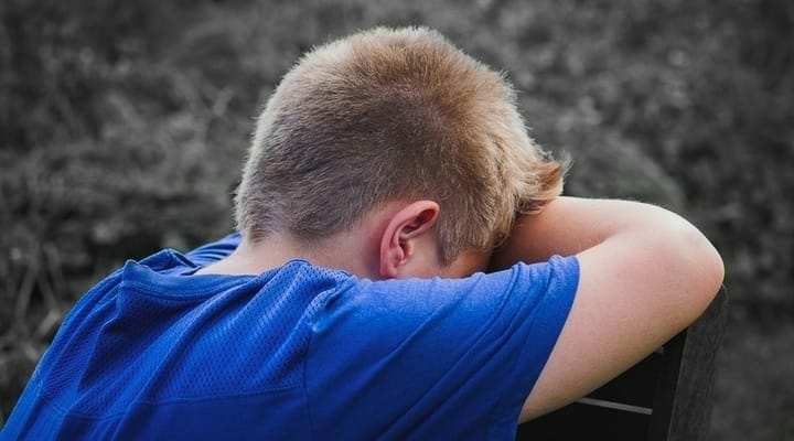 Criança de costas, encostada em um banco chorando.