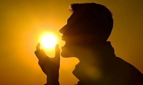 A foto mostra o sol e um homem fingindo pegá-lo com a mão para comê-lo, representando a obtenção da vitamina D pelo sol.