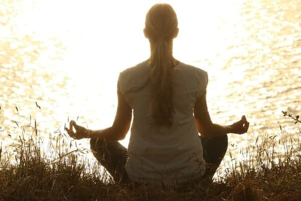 Foto de uma pessoa meditando na beira de um lago. A meditação representa uma atividade que exige muita concentração.