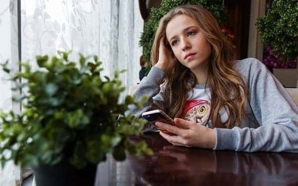 Adolescente com depressão, sentada à mesa com um celular na mão e olhando "para o nada"