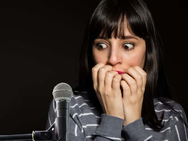 foto de uma mulher assustada olhando para um microfone, com medo de falar em público, sintoma da fobia social.