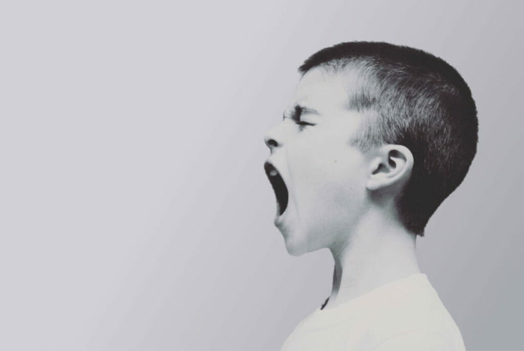 Foto de perfil de um menino gritando, representando a agressividade, um dos sintomas do transtorno de estresse pós-traumático em crianças