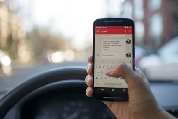 Foto de dentro de um carro, representando um motorista dirigindo e mexendo no celular.